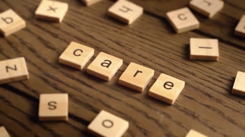 Hand Places Wooden Tiles to Spell Care on Rustic Wooden Surface