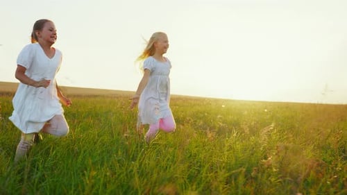 Girls Running Happily Through Grassy Field at Sunset