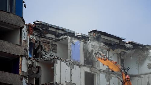 Excavator claw breaks the parts of ruined building.