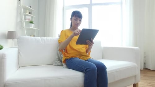 Woman Sitting on Couch Using Tablet in Bright Room