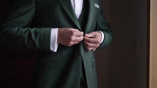 Man buttoning his green suit jacket, wearing a wedding ring and cufflinks in a formal setting