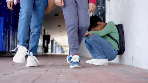 Caminhando no corredor da escola, estudantes passando enquanto a criança está sentada contra a parede