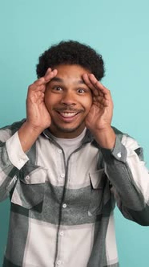 Stunned Young Man Smiling at Camera in Blue Studio