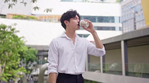 Asian young businessman drinking a cup of coffee while walking in city.