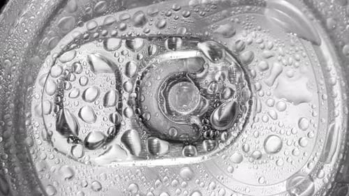 A close-up view of the top of a beverage can with water droplets.