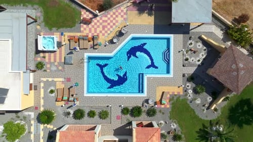 Birds eye drone shot above a woman swimming in a pool at a resort in sunny Greece
