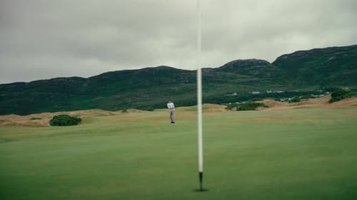 Male golfer hits chip shot onto putting green on Ireland Links golf course, ball bounces in slow mot
