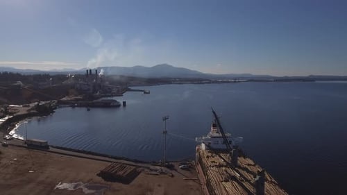 Imagens de drone em 4K de um porto madeireiro com um navio sendo carregado com troncos