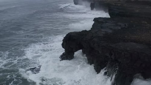 Drone top down of water hitting rocky cliff during cloudy day in Iceland