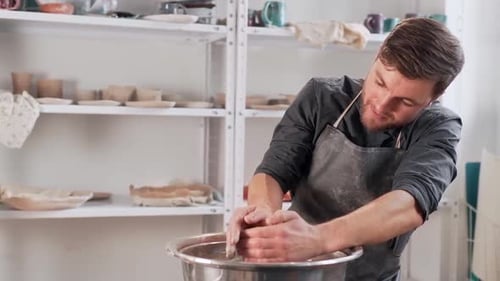 Focused pretty man working on pottery wheel over product