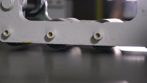 Folhas de metal finas em closeup se movem entre rolos rotativos