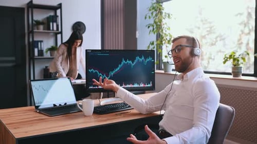 Der Börsenmakler sitzt am Computer mit Grafiken und spricht über Kopfhörer mit Mikrofon.