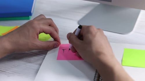 Mann schreibt Wort Task auf rosa Haftnotiz am hellen Holztisch, Nahaufnahme. Planung und Frist