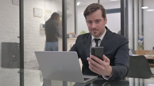 Man in Suit Uses Laptop and Phone in Office