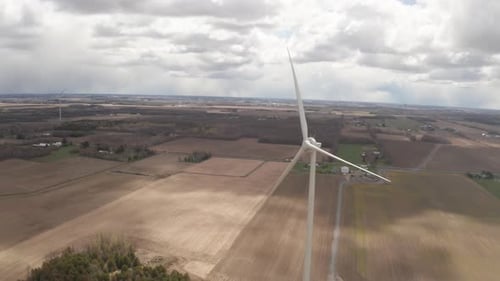 Drone flying past blades of wind power propeller not spinning. Dramatic sky over rural farm with bro