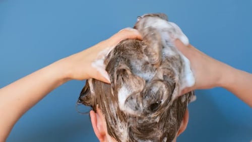 Girl washes her hair with shampoo on blue background, rear view.