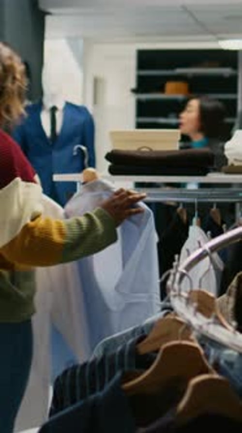 Vertical Video Modern Client Looking at Shirts Hanging in Clothing Store