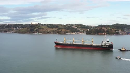 Cargo Ship Moving Through Water with Tugboats