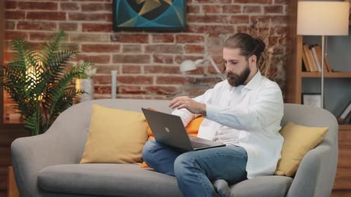 Man Typing on Laptop on Couch Indoors