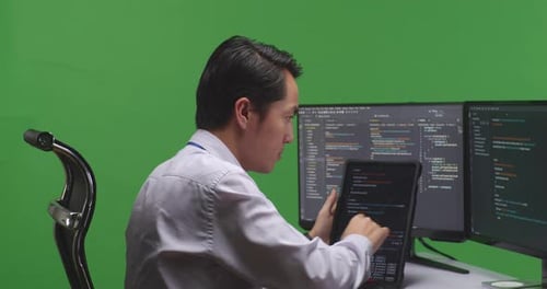 Man Developer Working With Tablet While Write Code With Multiple Computer Screens In Green Screen
