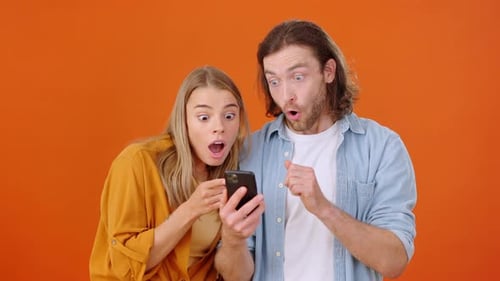 Excited Couple Looking at Phone as Money Falls