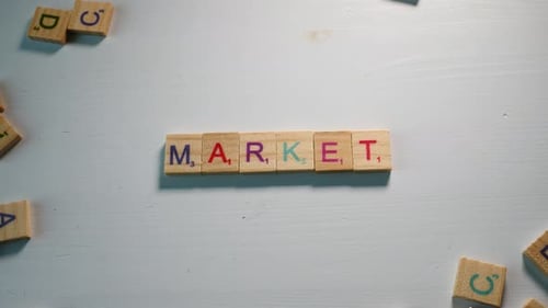 A person adding the letter T to the word Market with wooden letters on a white background with other
