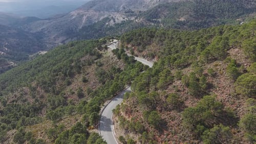 A breathtaking aerial view of a winding mountain road cutting through a vast forested landscape.