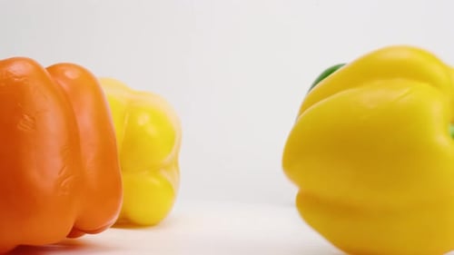 Buntes Medley aus roten, orangen, gelben und grünen Paprikaschoten, die auf eine weiße Tischplatte fallen und abprallen