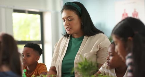 African American teacher looking left, speaking, guiding students with potted plants, green bottle