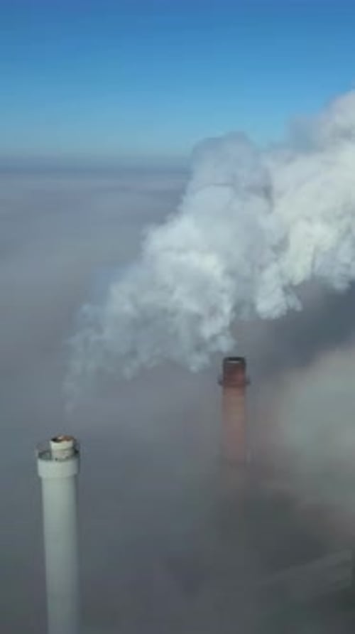 Thick industrial smoke rising from factory chimneys in a clear blue sky