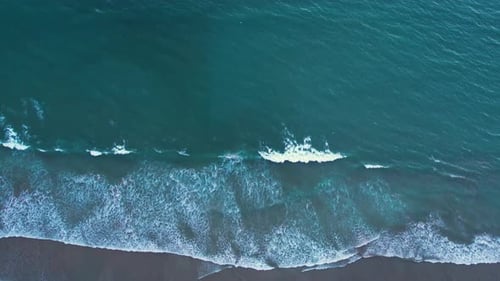 Aerial shot of foamy waves washing onto a sandy beach