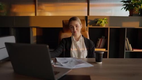 Portrait of a Confident Blonde Girl in a Business Uniform Who Sits at a Wooden Table in the Office