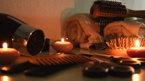 Primer plano de herramientas de peluquería, cepillos, tijeras, peines, secador de pelo, toallas, junto a algunas velas