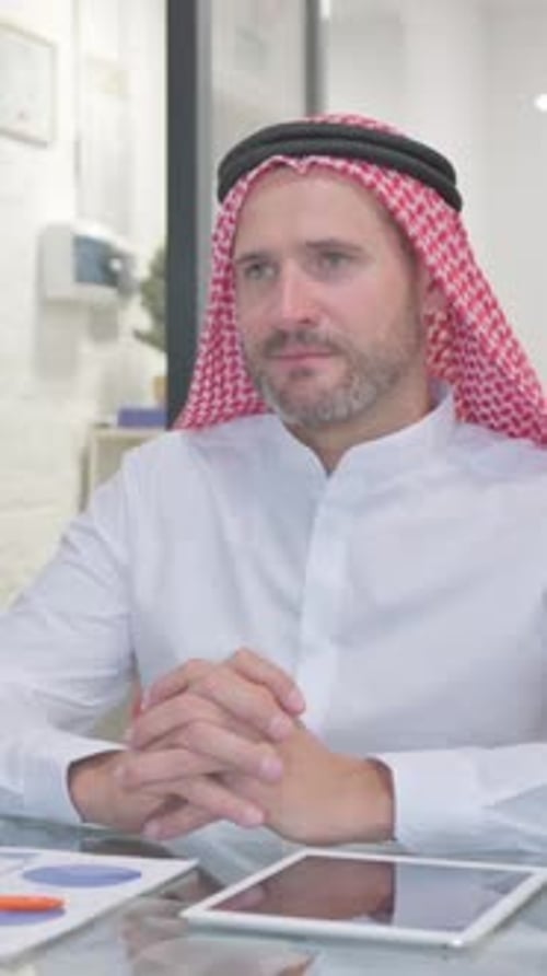 Man Wearing Keffiyeh Sits at Desk with Tablet