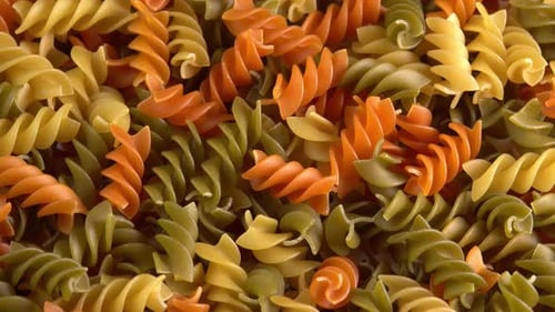 Multicolored italian pasta Fusilli or Rotini rotating background closeup top view side light