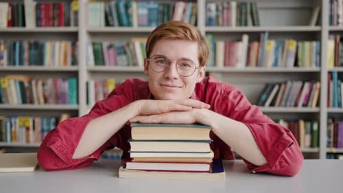 Young Student Smiling in Library with Stack of Books