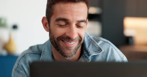 Man Smiles Looking at Laptop Screen at Home