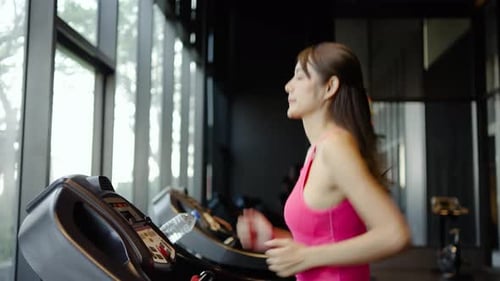 Young girl jogging on a treadmill in a gym, side view, Muscular athletes actively training in gym