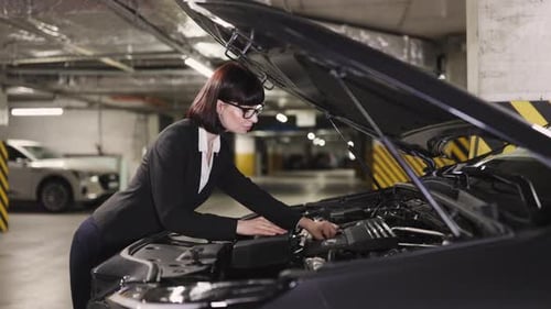 Caucasian Businesswoman Repairing Car Engine in Underground Parking Garage