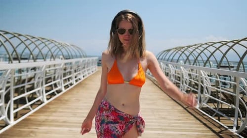 A beautiful slender girl walks dancing along a picturesque wooden bridge on the sea