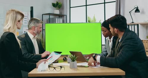 Man and woman business partners working together in modern boardroom near green chroma screen