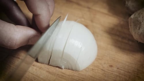 Person Chopping White Onion Using Sharp Kitchen Knife Into Wooden Chopping Board. - Close Up Shot