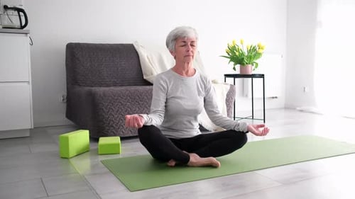 Senior Woman Meditating at Home on Yoga Mat