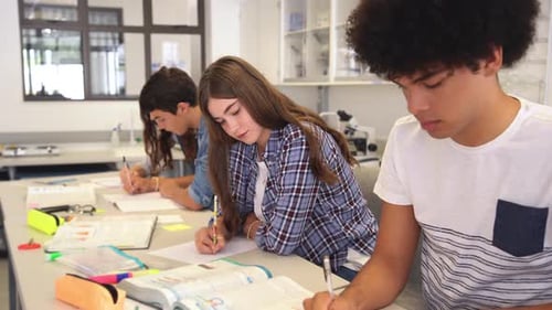 Group Of College Students Studying In Classroom Writing Notes During Lesson. Focused Guy And Girl...