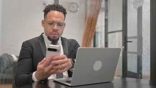 Professional Man Using Phone and Laptop at Desk
