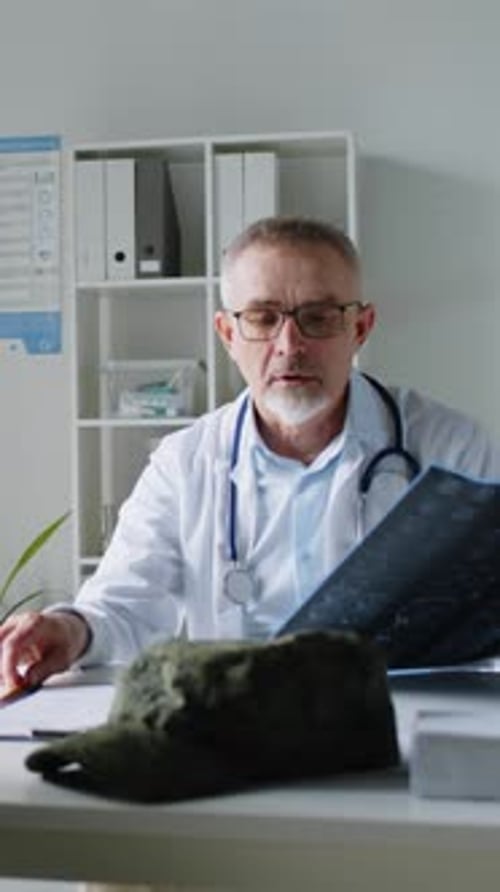Male Physician Explaining Diagnosis to his Patient by Showing X-ray in Clinic