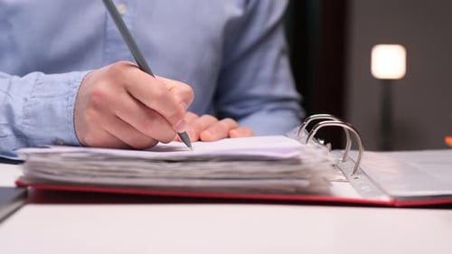 Office Worker Writing Notes on Paper in a Binder at Night