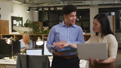 Biracial man and Asian woman discuss business work in an office