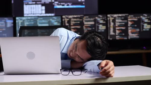 Programmeur endormi pendant l'écriture de code par un ordinateur portable utilisant plusieurs moniteurs affichant la base de données