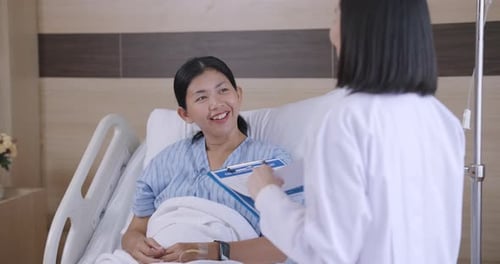 Close up asian female patient smiling and looking up during hospital room interaction with female